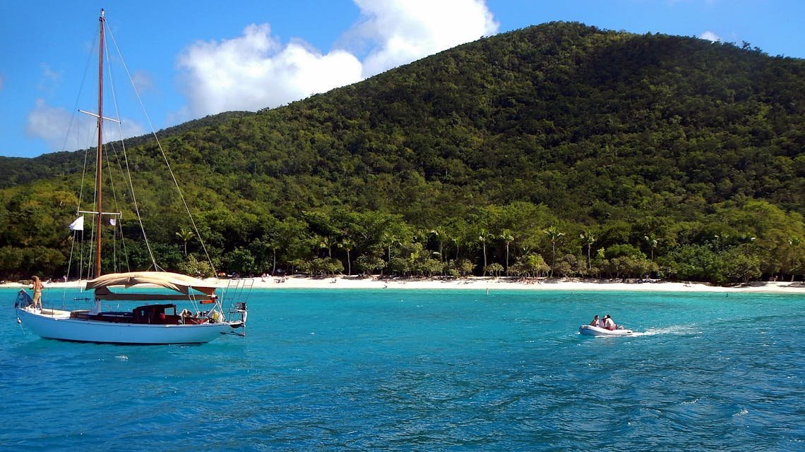 Scenic view of a sailboat and motorboat near the shore of St. John's lush beaches, perfect for a tropical vacation.