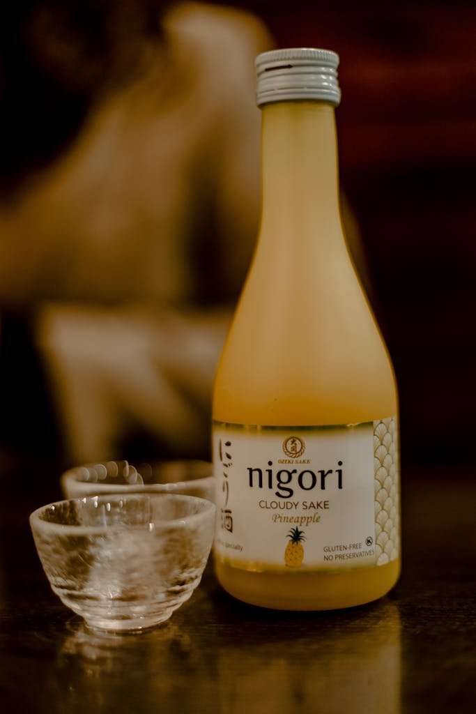 A bottle of pineapple nigori sake served with sake glasses on a wooden table.
