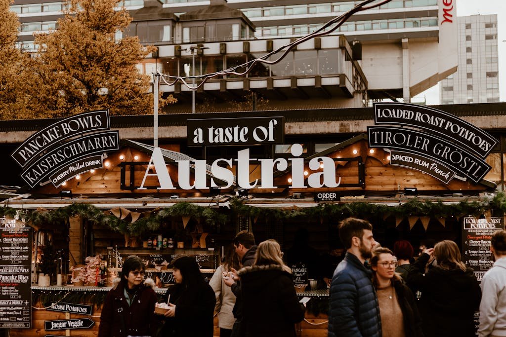 A bustling Austrian food market stall offering traditional delicacies and drinks in an urban setting.