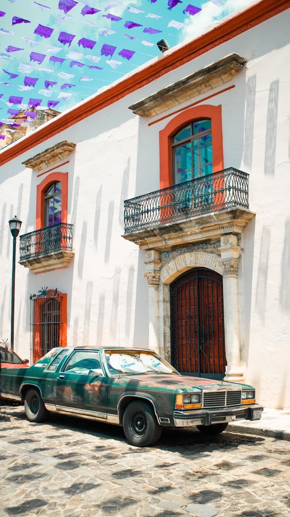 A classic vintage Ford car parked in the vibrant streets of Oaxaca, Mexico, under colorful decorations.