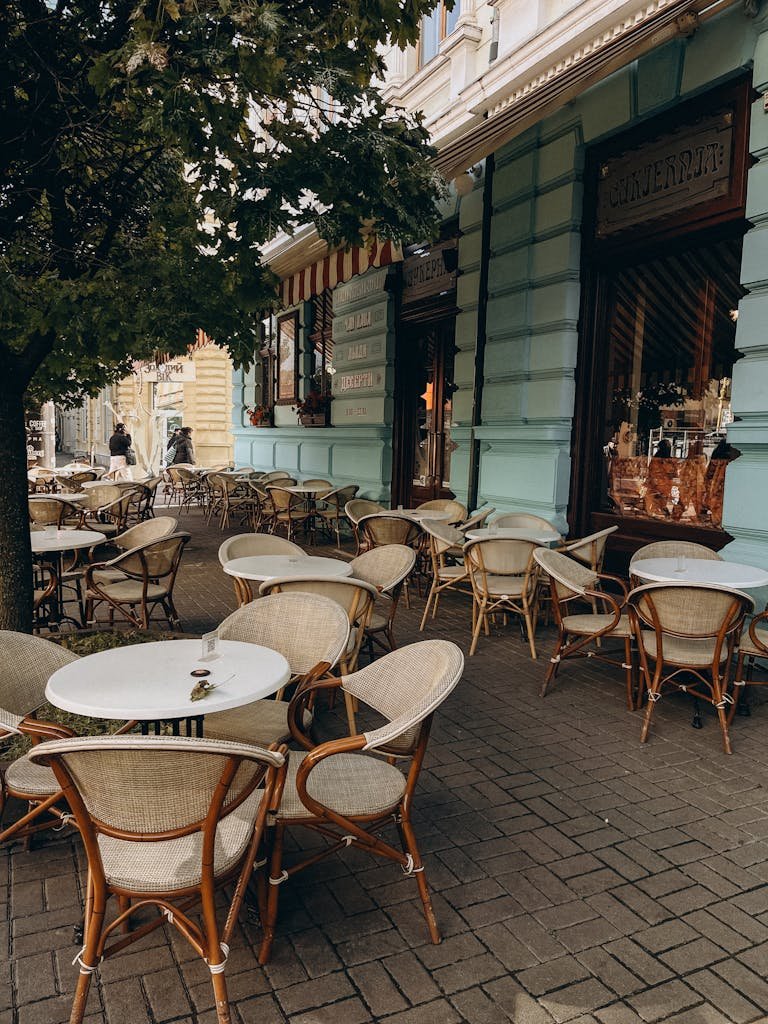 A delightful outdoor café with wicker chairs and tables on a cobblestone sidewalk, perfect for urban leisure.