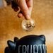 A hand places a Bitcoin into a piggy bank labeled 'Crypto', symbolizing savings and investment.