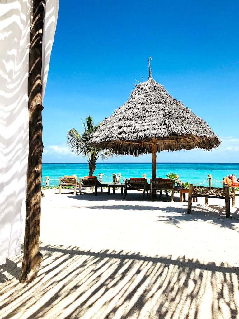 A serene tropical beach scene in Zanzibar featuring a straw umbrella and clear blue skies.