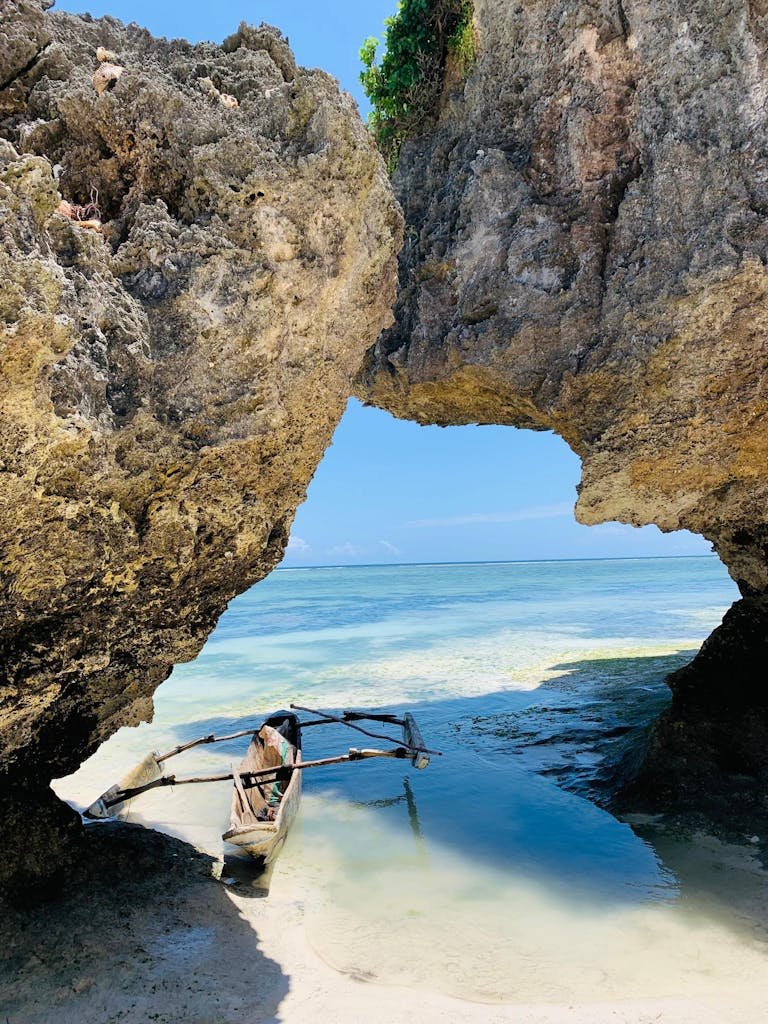 A traditional wooden boat docked in a serene tropical beach cove under large rock formations.
