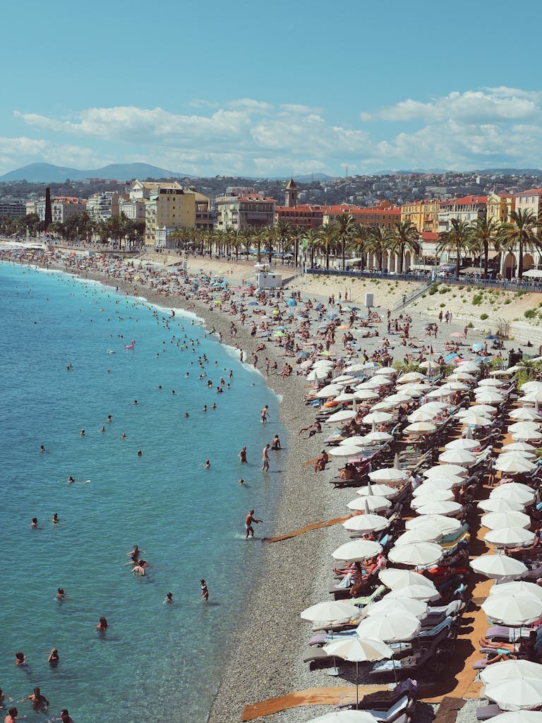 A vibrant aerial shot of Nice's bustling beach with sunbathers and umbrellas lining the shore.