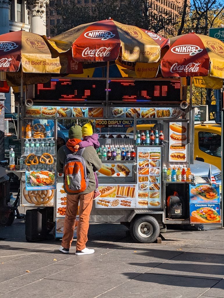 A vibrant New York City street food cart with customers on a sunny day.