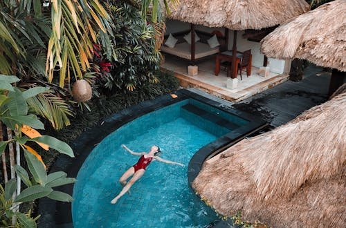 A woman enjoying leisure time floating in a tropical resort pool surrounded by lush greenery.