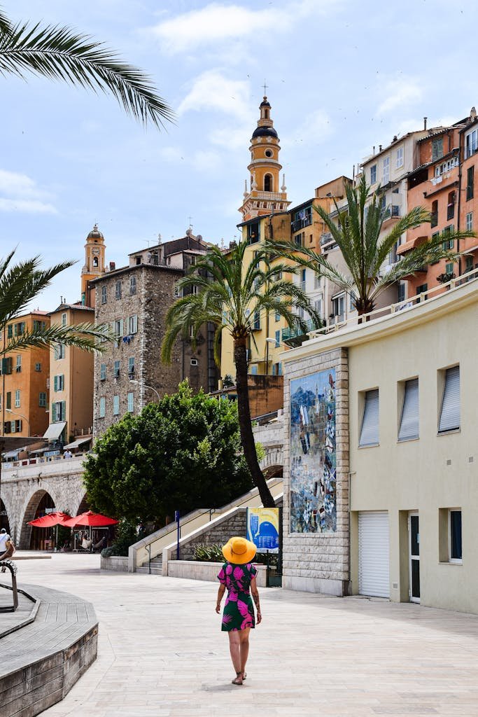 A woman walks along the vibrant streets of Menton in the French Riviera, showcasing Mediterranean architecture.
