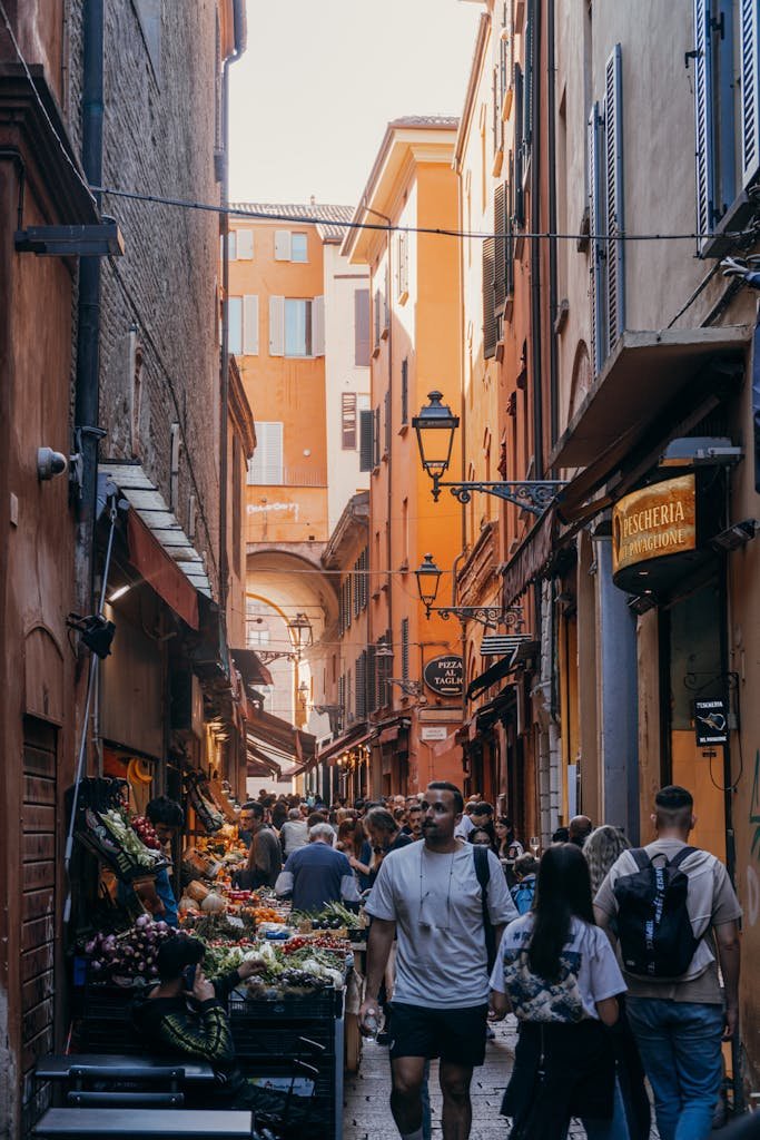 Bustling alleyway in Bologna's historic center with vibrant markets and crowds of people.