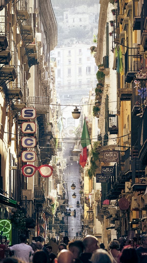 Bustling narrow street in Naples with vibrant buildings and Italian flags, capturing the essence of urban life.