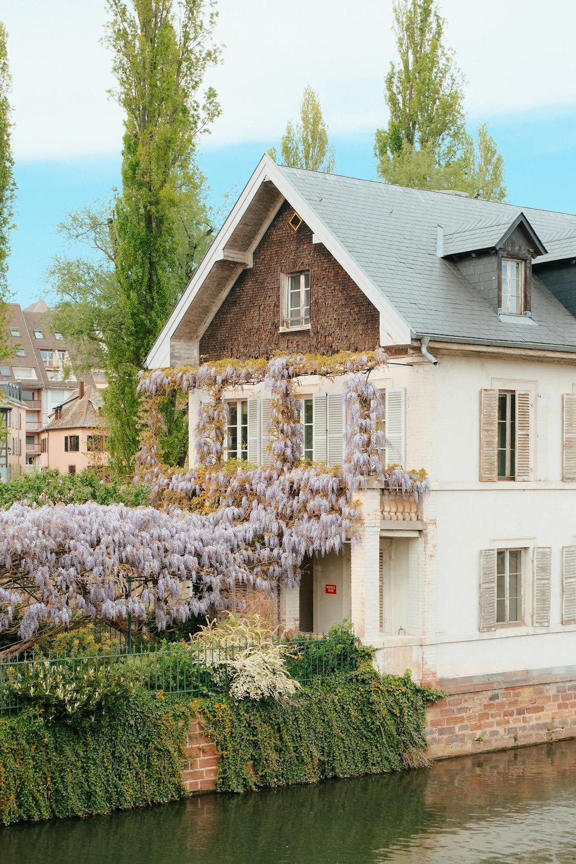 Charming house with wisteria in bloom beside a canal, showcasing classic French architecture.