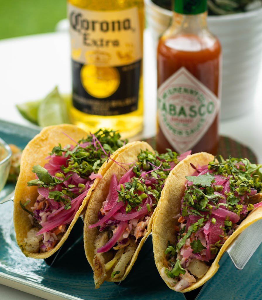 Close-up of vibrant Mexican tacos topped with fresh garnishes, accompanied by beer and hot sauce.