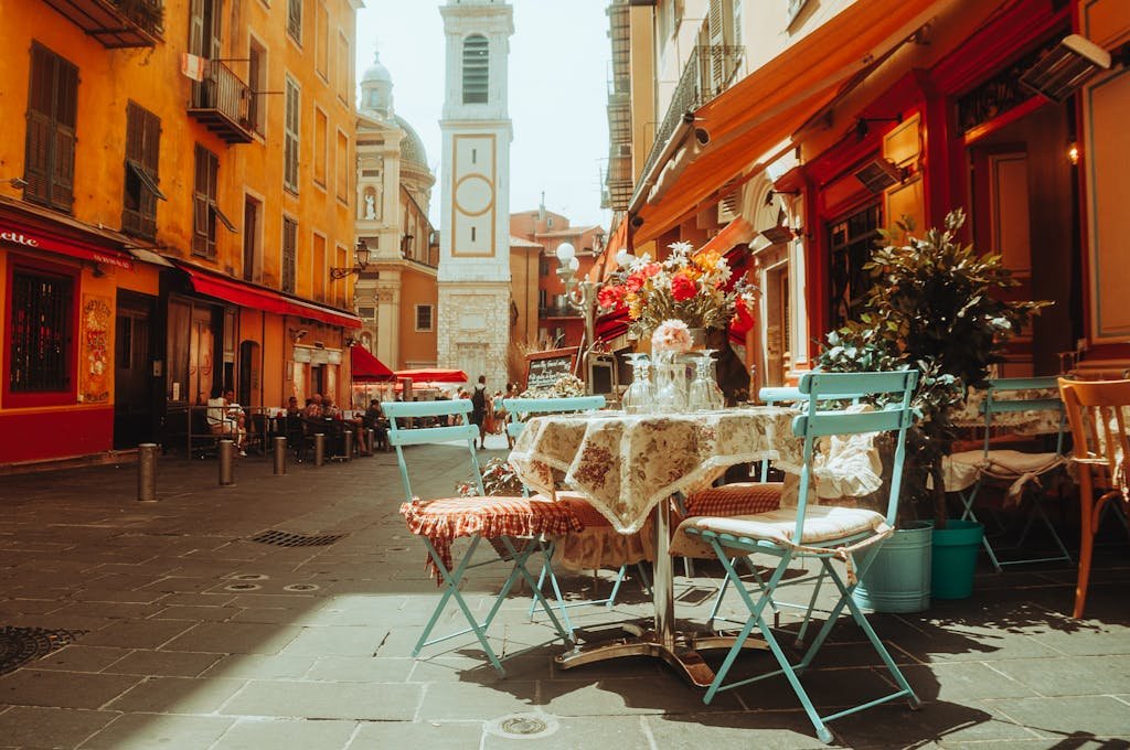 Colorful French café terrace with tables, flowers and church tower on sunny city street.