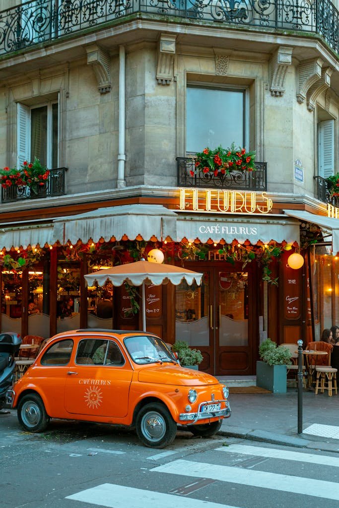 Colorful street view of a Paris café with an orange Fiat parked in front.