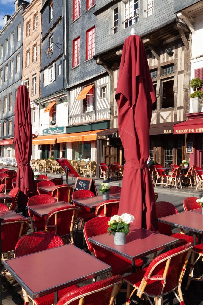 Cozy cafe terrace in Honfleur, France, featuring red tables and traditional architecture.