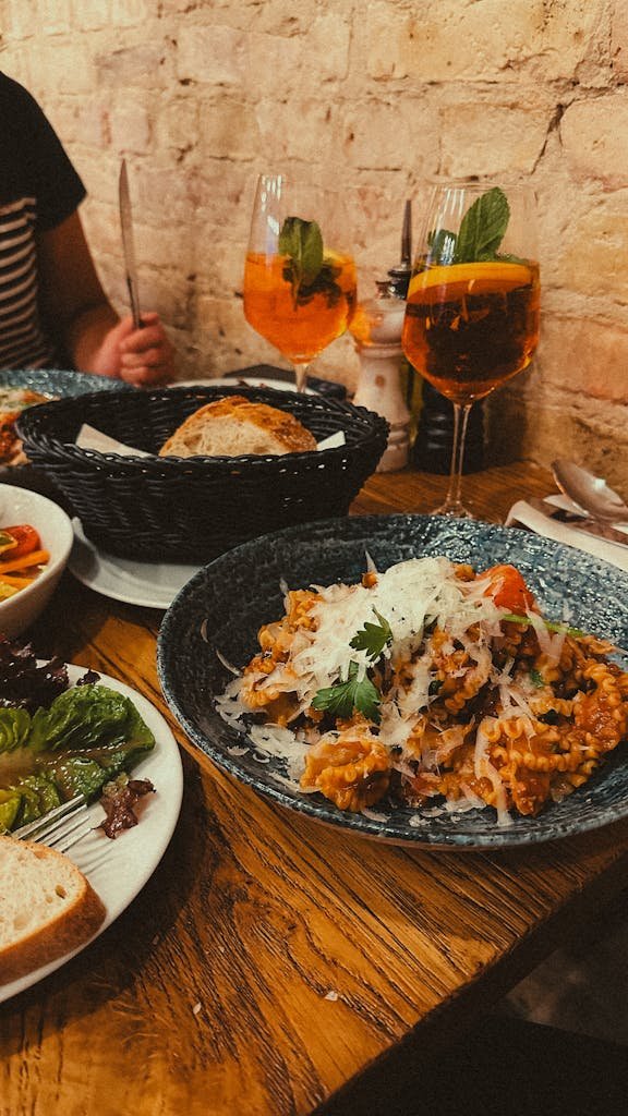 Cozy Italian dinner with pasta, salad, and Aperol Spritz on a rustic table setting.