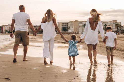 Family walking hand in hand along the beach at sunset, enjoying a warm summer day.