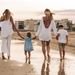 Family walking hand in hand along the beach at sunset, enjoying a warm summer day.