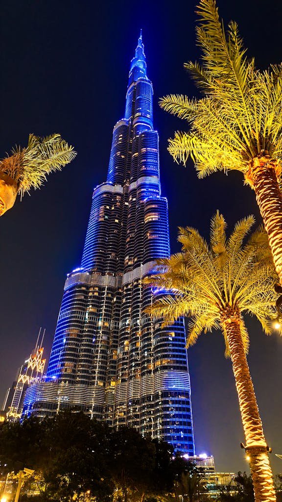 Illuminated Burj Khalifa with palm trees at night in Dubai.