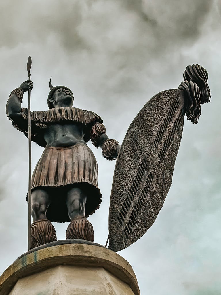 Impressive statue of a Zulu warrior with spear and shield under a cloudy sky.