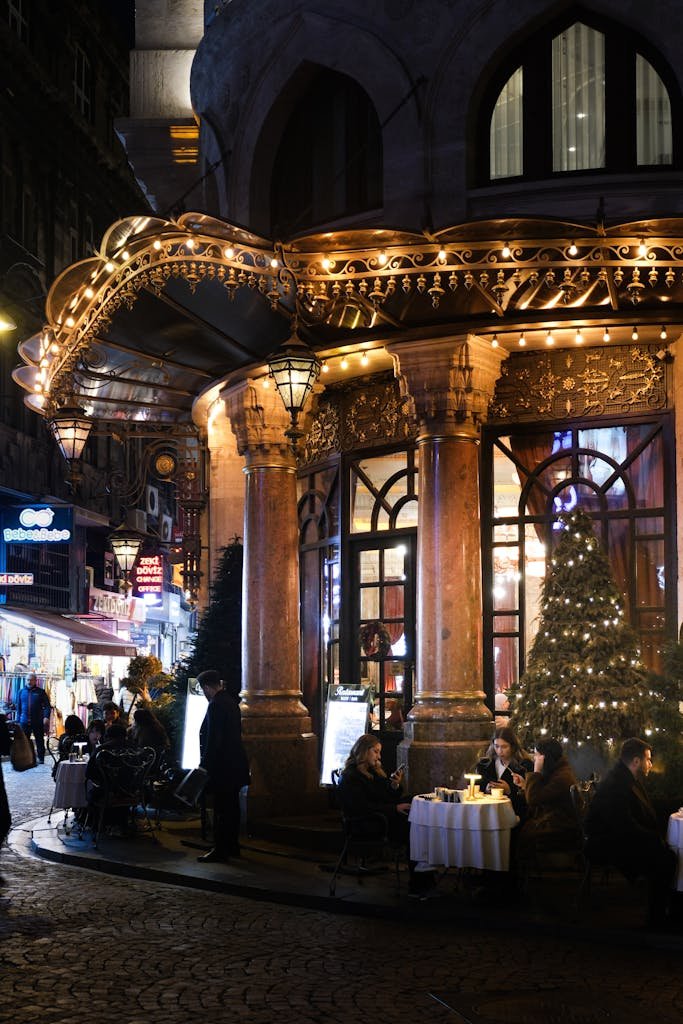 People dining at a warmly lit outdoor cafe at night.