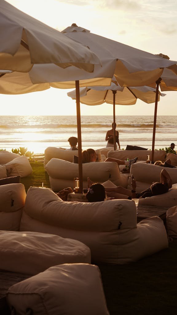People lounging under umbrellas at sunset by the beach, creating a serene and relaxing atmosphere.