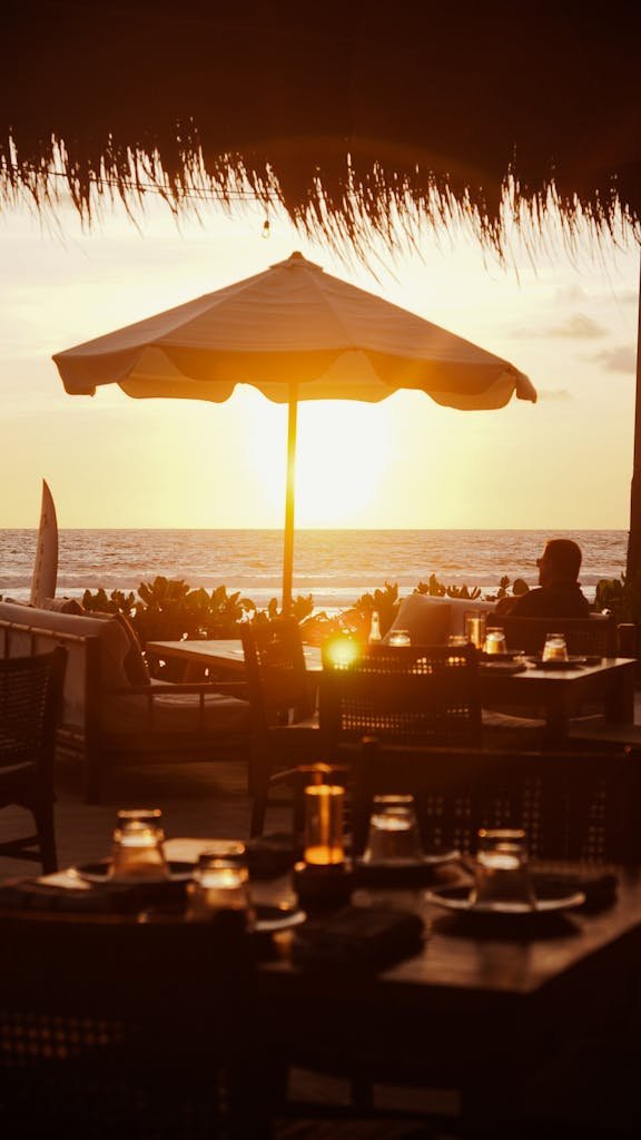 Relaxing beachfront restaurant scene at sunset with candlelit tables and ocean view.