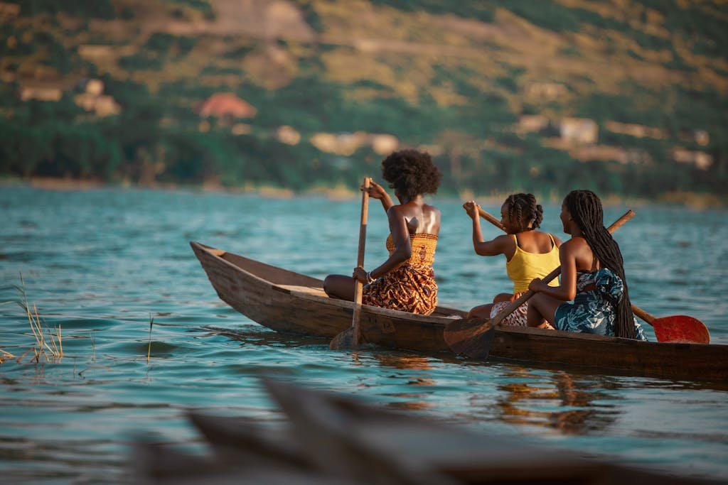Three women paddling a canoe on a scenic river in Accra, Ghana.