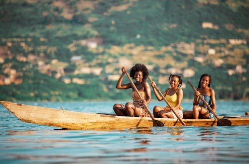 Three young women paddling a boat on a serene river in Accra, Ghana.