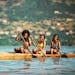 Three young women paddling a boat on a serene river in Accra, Ghana.