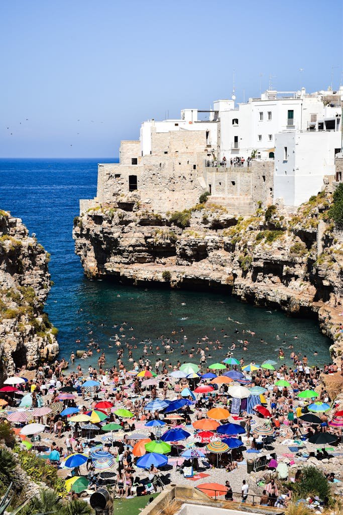 Vibrant beach scene at Polignano a Mare, Italy with colorful umbrellas and iconic cliffs.