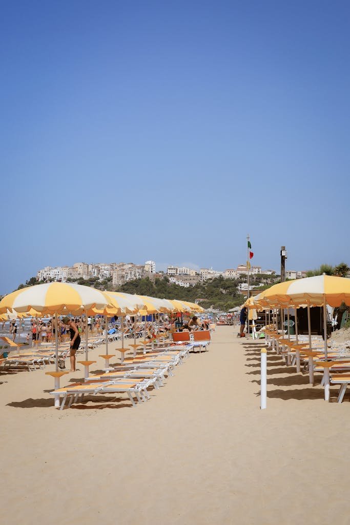 Vibrant beach scene with yellow umbrellas, loungers, and a distant view of a town.