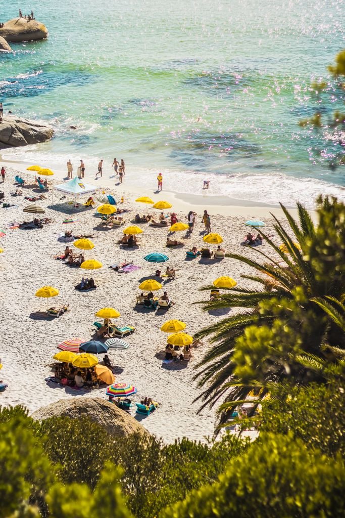 Vibrant summer day at Clifton Beach, Cape Town, with sunbathers and colorful umbrellas.