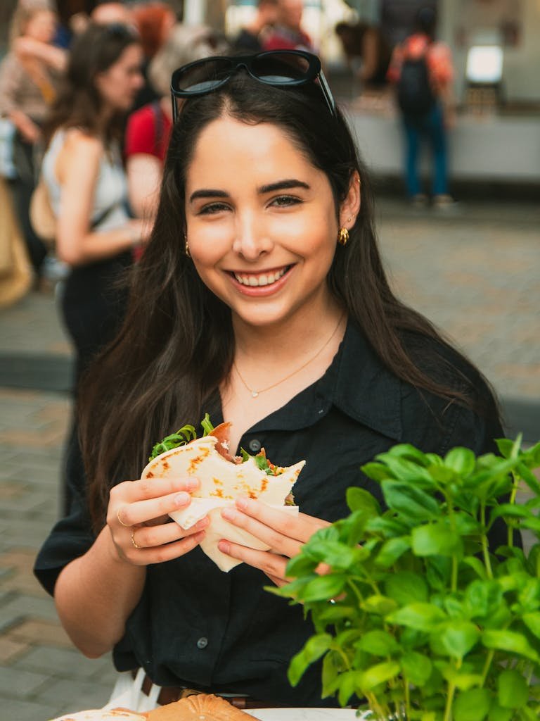 Young woman smiling and eating street food at an outdoor venue in Berlin.