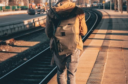 A man with a backpack walks along a train platform, capturing a journey moment in urban daylight.