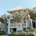 Sunny beach house exterior surrounded by lush palm trees and blue sky.