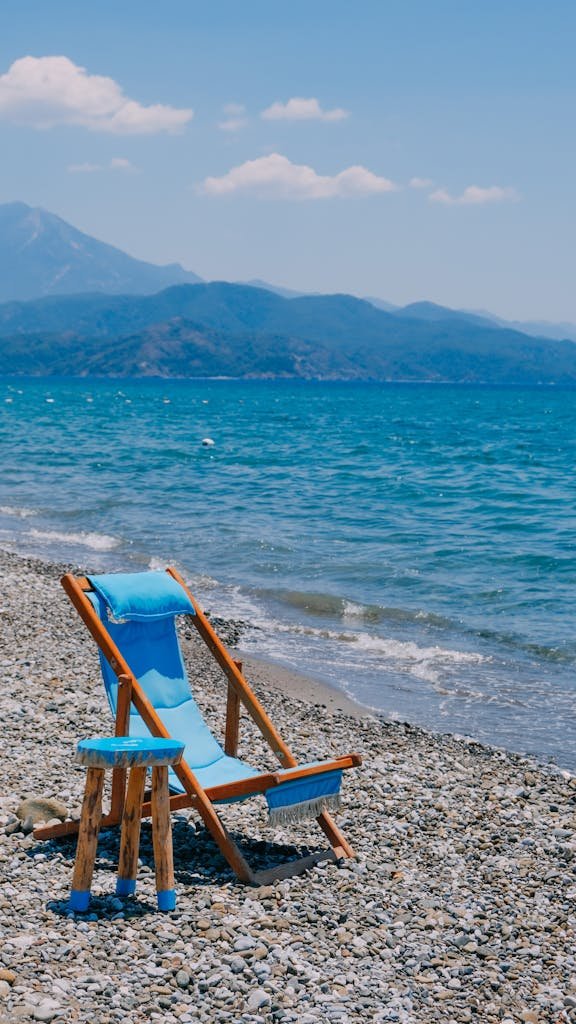 Tranquil pebble beach with a wooden lounge chair and vivid blue sea under a clear sky.